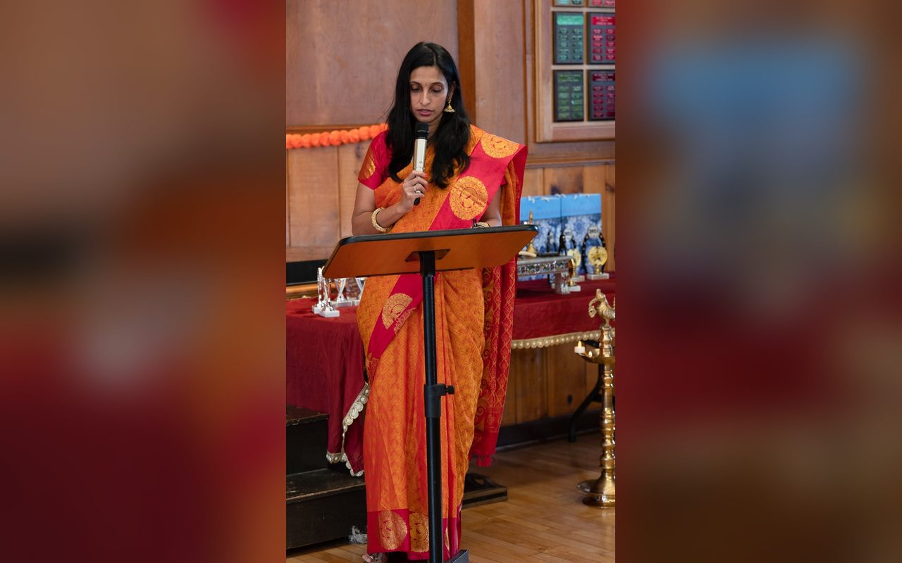 A speaker in an orange sari addresses the audience from a lectern