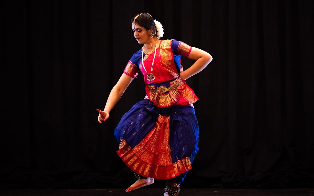 A dancer in red and blue holds a deep pose with one arm extended