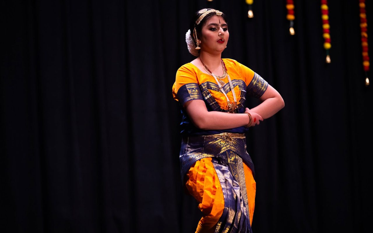 A dancer in a yellow and blue costume performs an expressive gesture