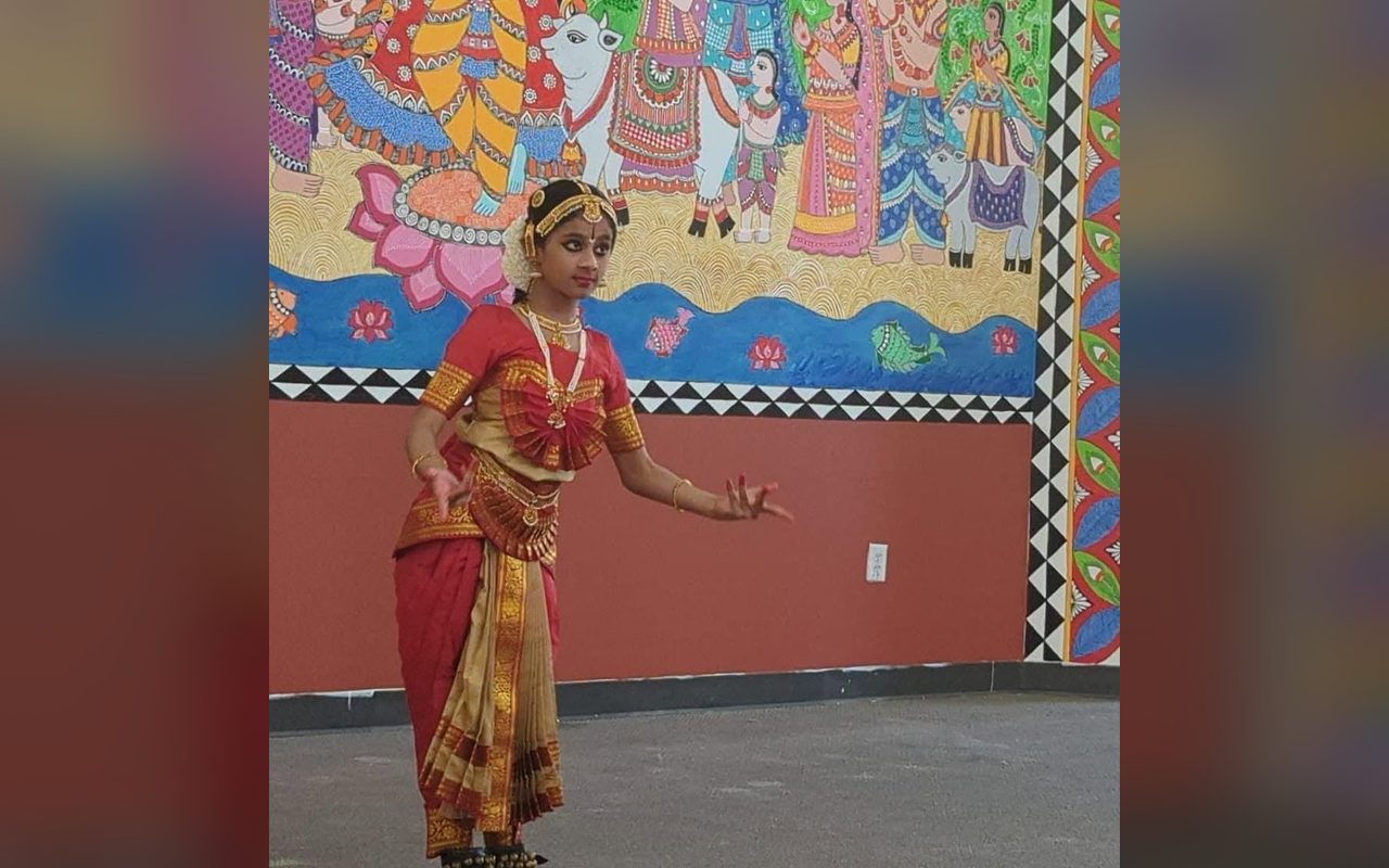 A dancer in red and gold performs in front of a mural of dancers and musicians