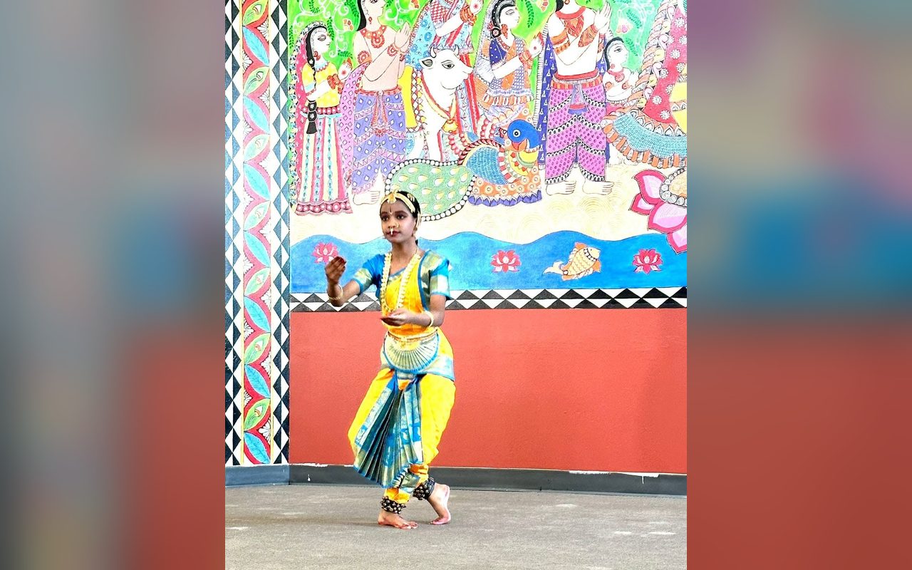 A young dancer in yellow and blue strikes a pose beneath a vivid wall mural