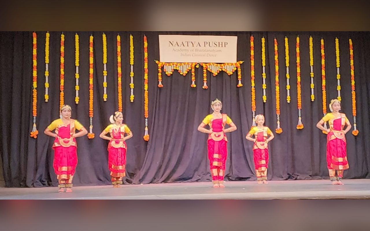 Dancers in pink costumes stand in formation beneath the Naatya Pushp banner