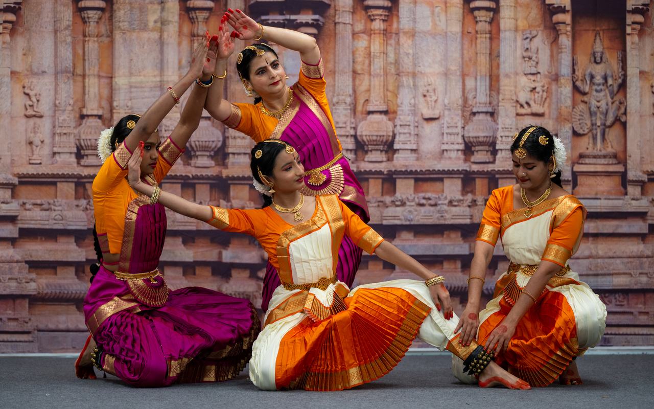 Four dancers in orange and magenta costumes form a sculptural group pose